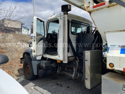 Mack GU713 dump truck cab with open door showing driver's seat and exposed engine area; side exhaust stack visible; cargo bed raised; VIN plate not legible.
