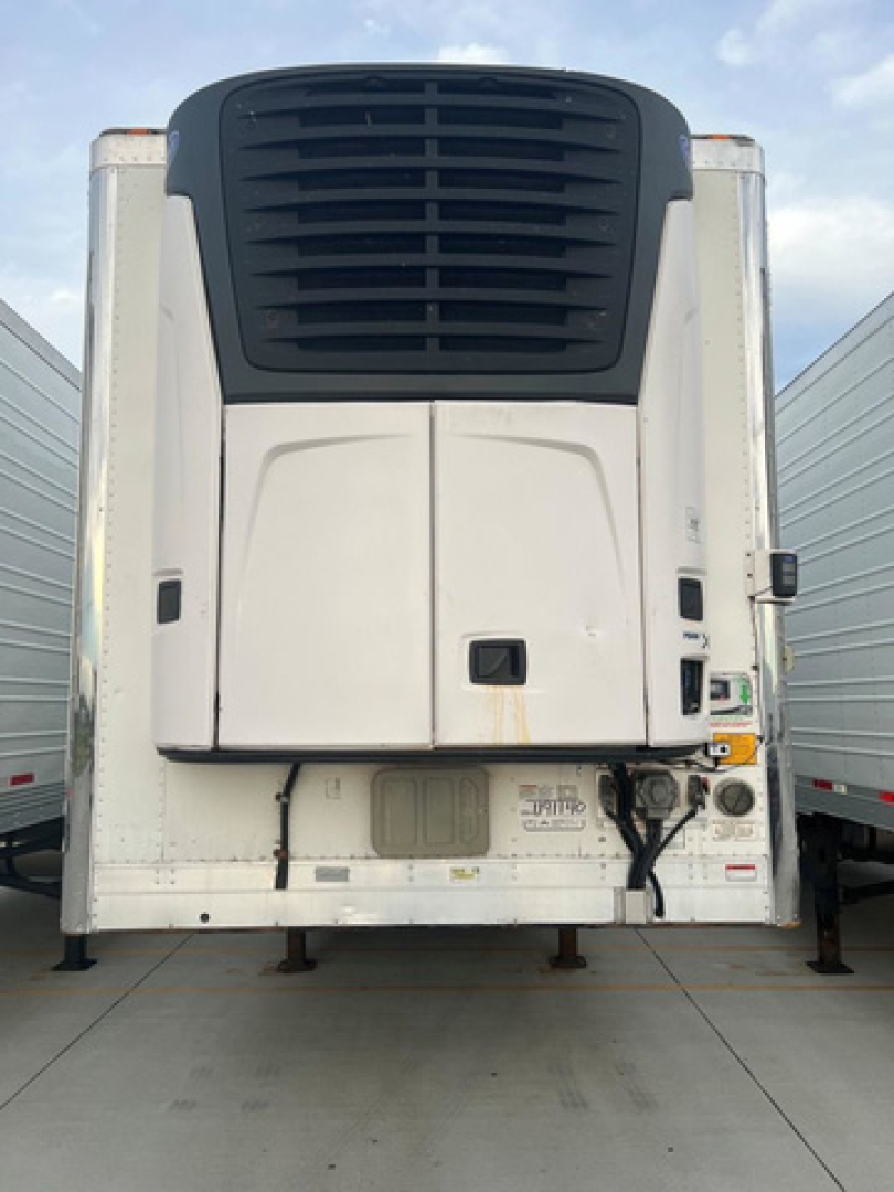 Utility reefer trailer rear view showing large black cooling unit, white curtainsides, and various control panels with stickers and labels.
