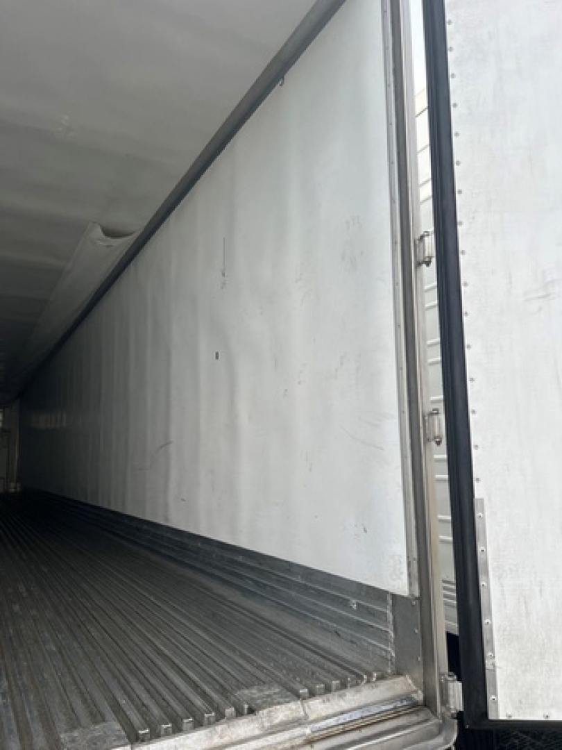 Trailer interior showing empty refrigerated box with metal walls and ribbed floor, side door open, utility reefer unit inside.