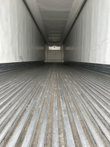 Interior view of a refrigerated trailer showing ribbed floor and side walls with a rear doorway visible at far end.