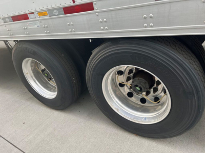 Trailer axles and dual rear tires of a 2021 Utility refrigerated trailer showing two wheels with polished rims and tire treads.