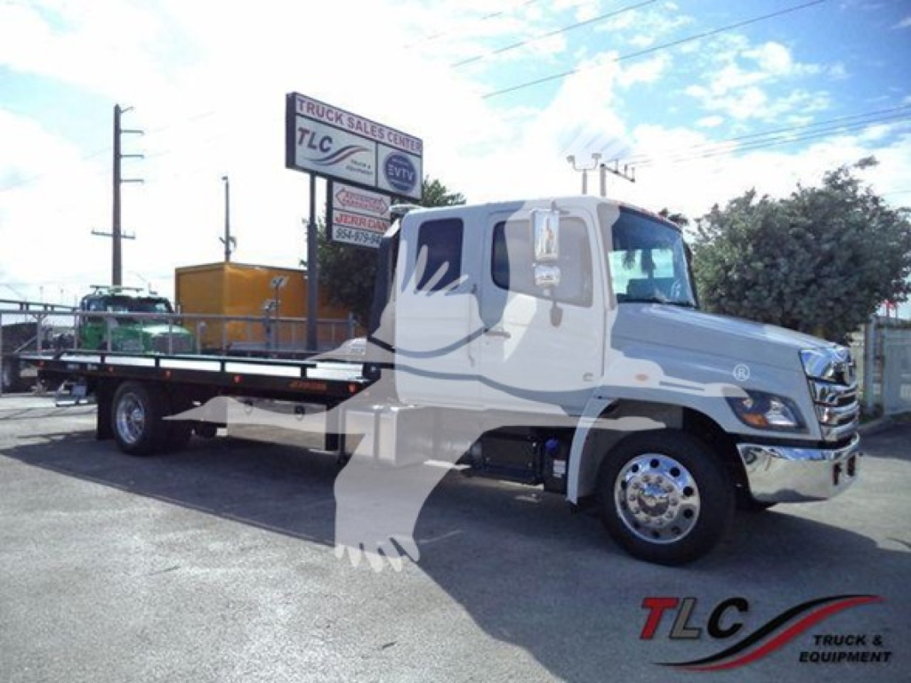 Truck bay showing a white Hino 268A rollback tow truck with a flatbed, chrome bumper, and logos; dealership sign in background.