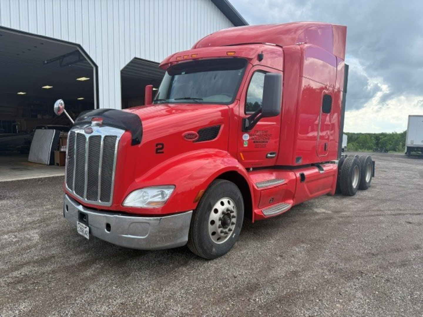 Peterbilt 579 tractor in red, front-left view, with sleeper cab and dual rear axles. Visible Peterbilt emblem on grille, chrome bumper, and side mirrors.