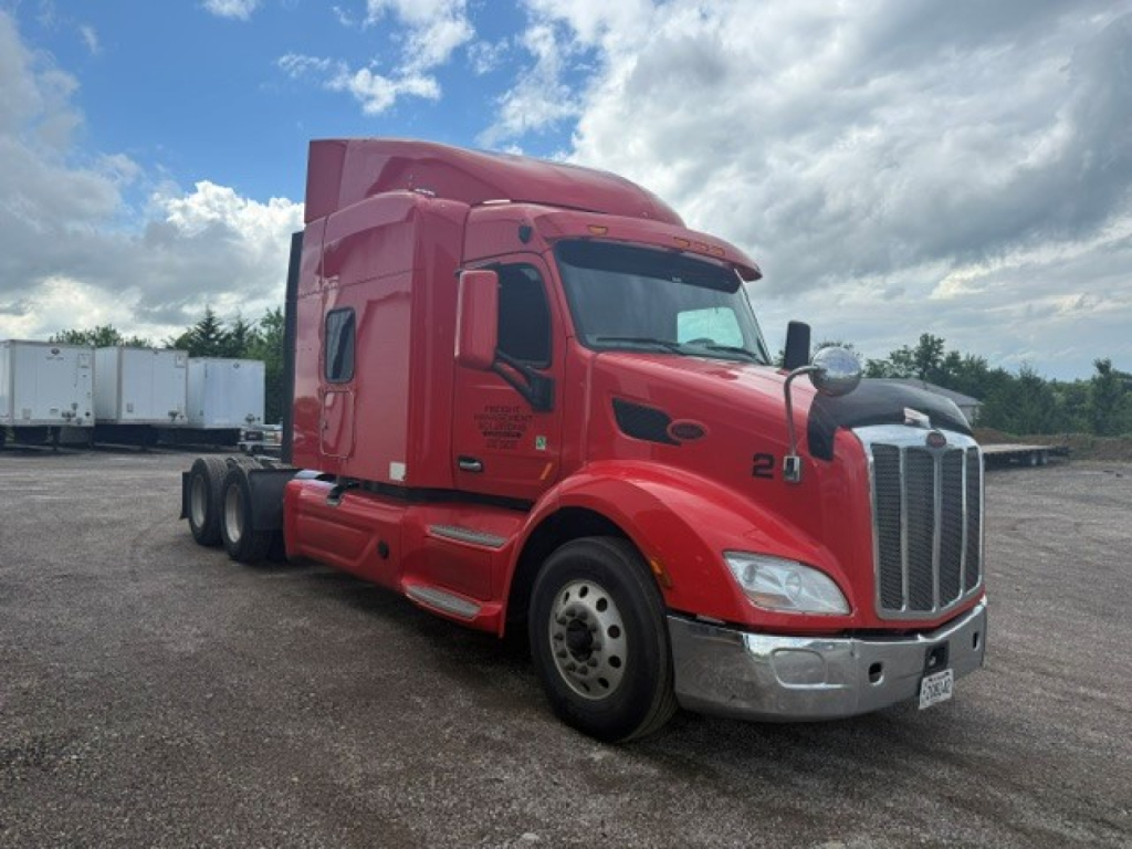 Peterbilt 579 sleeper cab tractor in red, front-left view, with chrome bumper and large grille, displayed in a gravel lot.