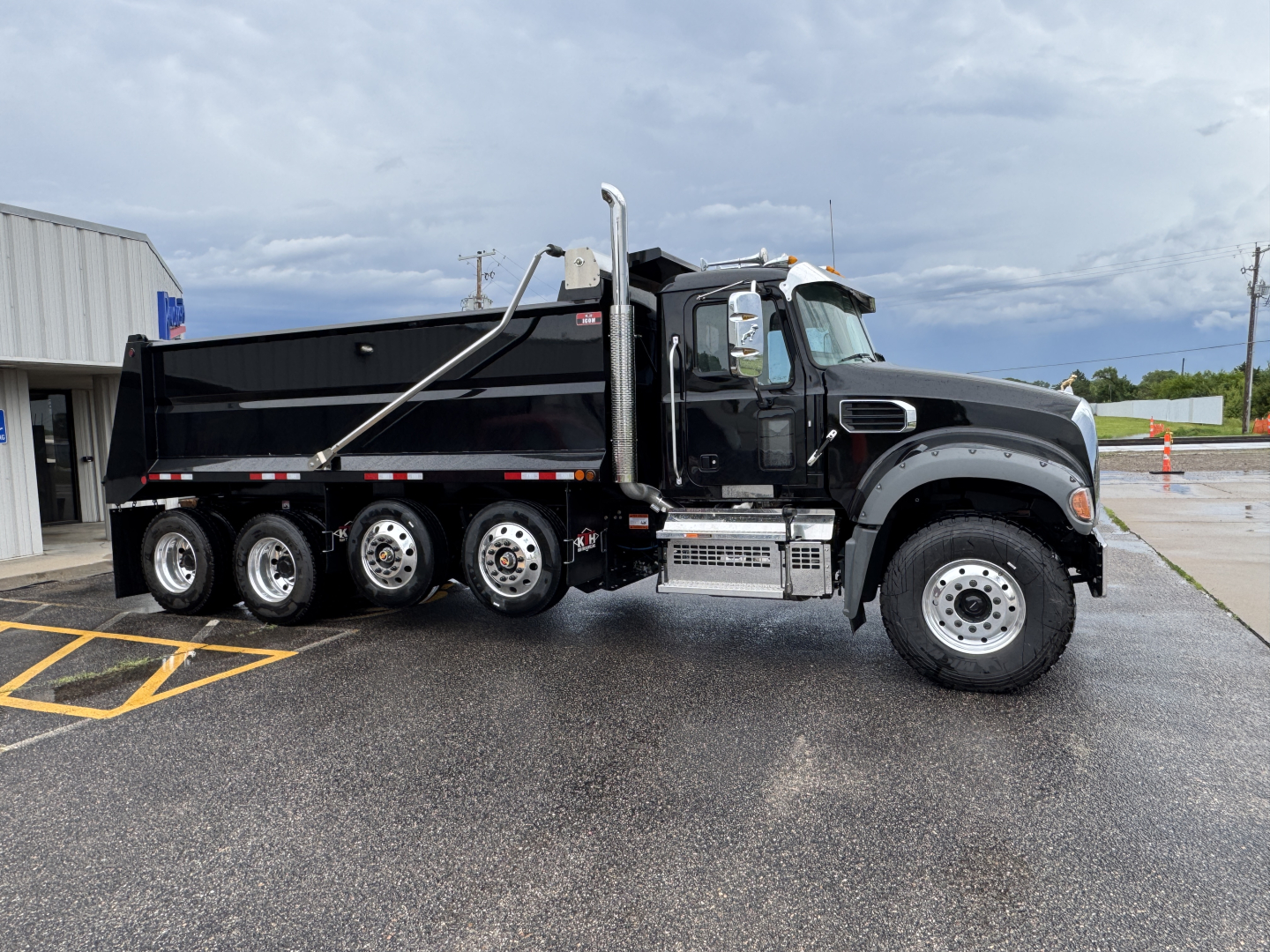 Truck side view of a new 2025 Mack GR104F dump truck showing black dump bed, dual rear wheels, chrome step, and VIN/stock listed in header