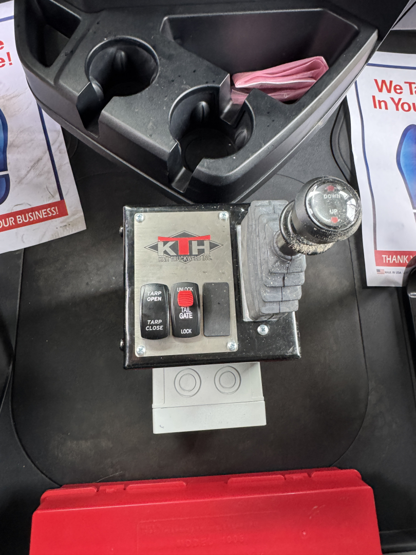 Dashboard area with control panel labeled KTI? showing jumper switches, two cup holders, and a lever with a round knob; surrounding consoles and a red storage bin.