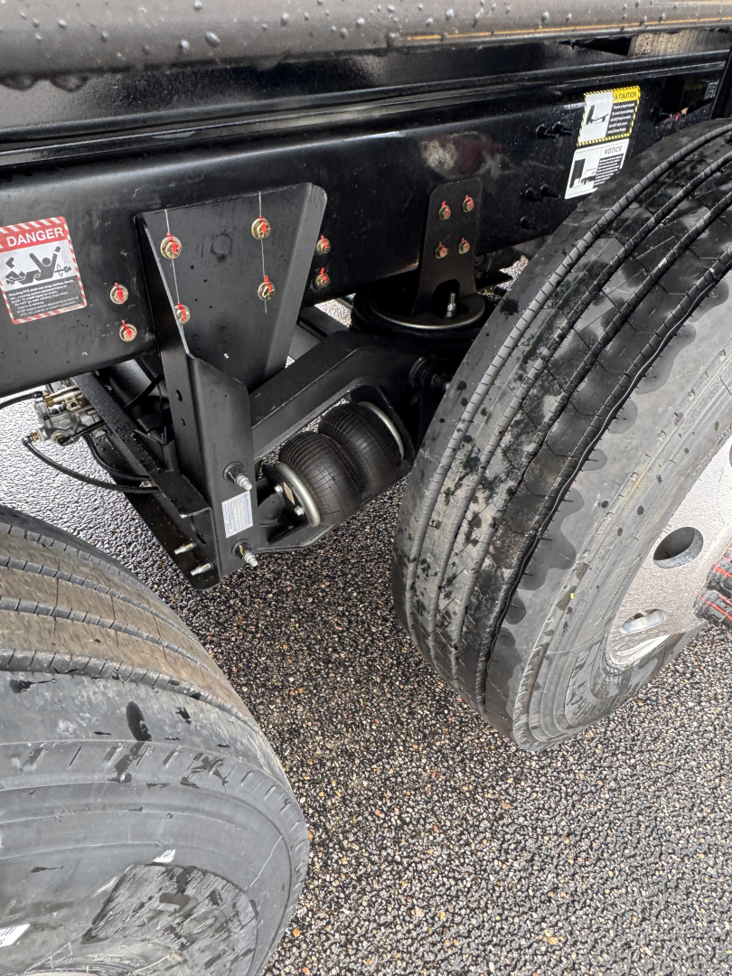 Mack GR104F dump truck chassis showing dual rear axles and suspension components with tires and warning labels visible.