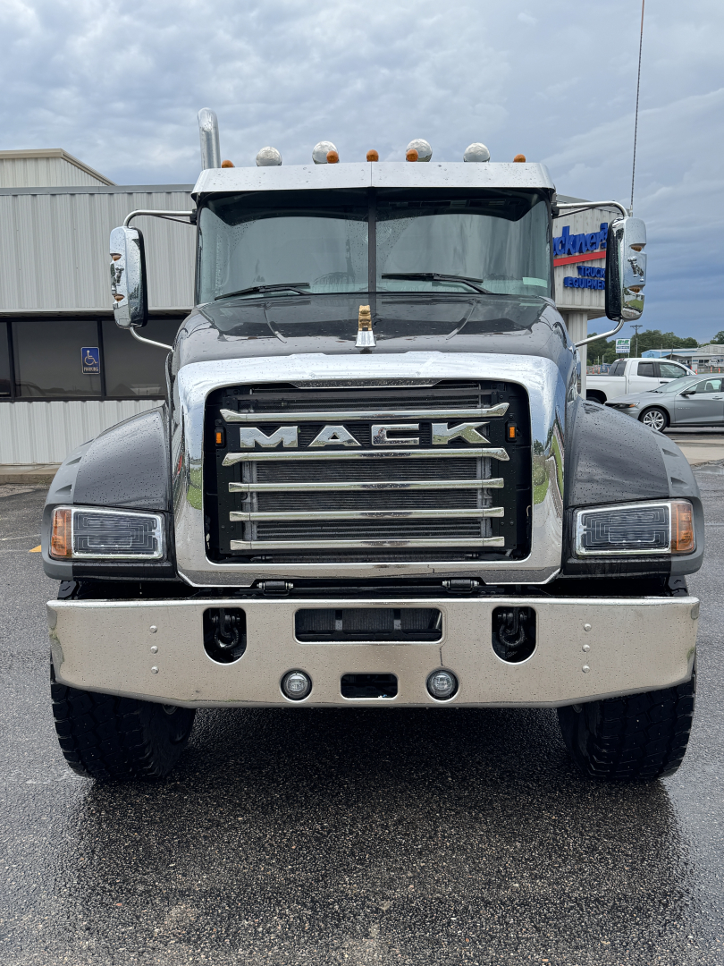 Front view of a Mack dump truck showing grille with MACK emblem, chrome bumper with lights, and large tires.