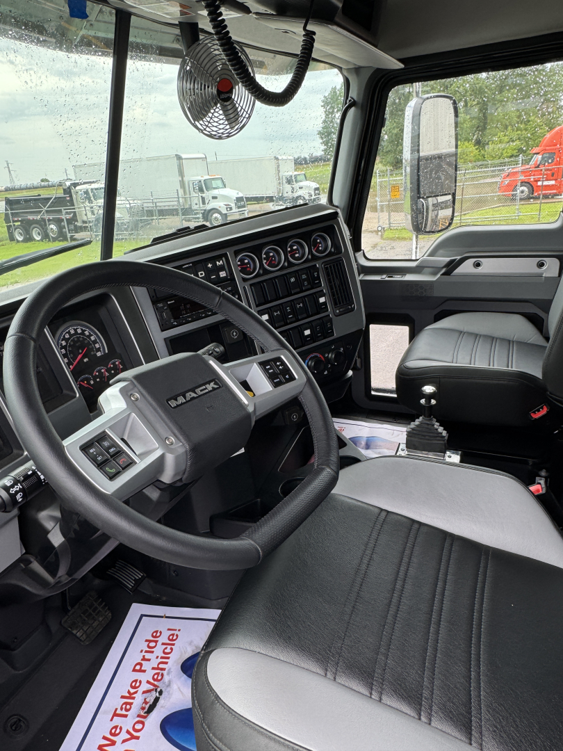 Interior view of a new 2025 Mack GR104F dump truck cab showing steering wheel, instrument cluster, and driver seat with dashboard controls.