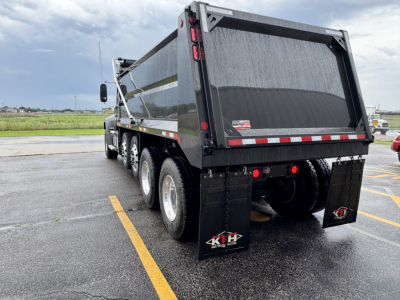 Dump truck rear view showing black dump bed with reflective tape, triple rear axles, mud flaps, and tailgate. Visible branding: 4KH mud flaps.