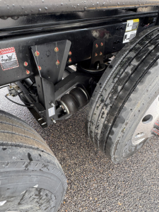 Mack GR104F dump truck chassis showing dual rear axles and suspension components with tires and warning labels visible.