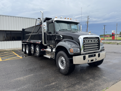 Dump truck showing Mack GR104F cab with chrome grille and dual exhaust stacks; front view; black body with chrome bumper and multiple rear axles; VIN plate not visible.
