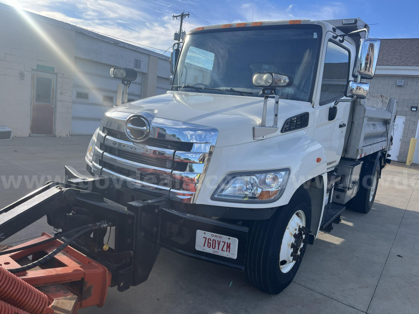 Hino 338 dump truck front-left view showing chrome grille, headlights, side mirrors, and dump bed with warning lights.