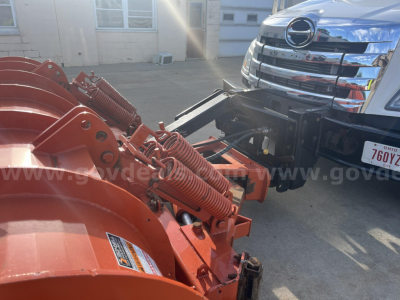 Front view of a 2012 Hino 338 dump truck connected to a red snowplow or hydraulic implement showing hydraulic cylinders and mounting brackets.