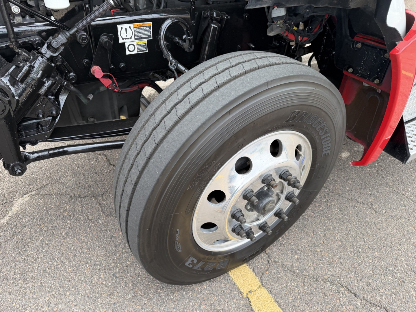 Front wheel of a Kenworth T880 conventional daycab showing dual tires and wheel hub with lug nuts; body components and underhood area visible.