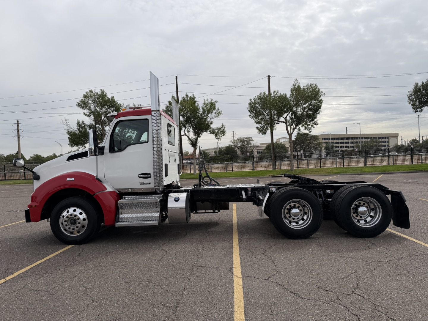 Kenworth T880 cab with red front end and white sleeper, side view showing chassis and dual rear axles, no trailer attached.