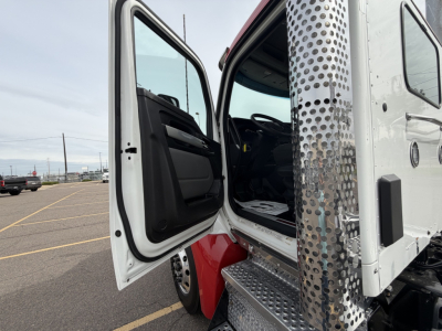 Kenworth T880 cab door open showing steps and interior, exterior chrome exhaust stack with perforated heat shield, white cab, red fenders.