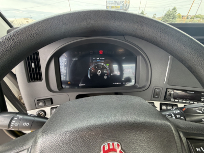 Kenworth truck cockpit with digital gauge cluster and steering wheel; various controls; dashboard text not fully legible.