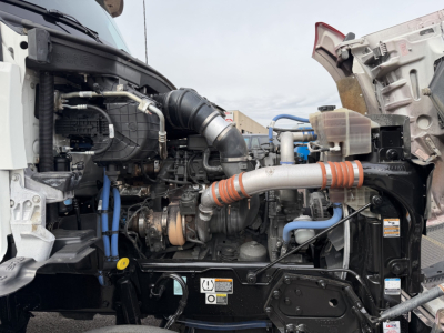 Kenworth truck engine bay with exposed turbocompressor, hoses, and coolant lines; front of a 2023 T880 with open hood showing engine components and auxiliary equipment.