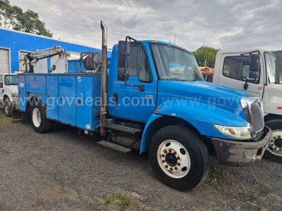 Blue 2004 International 4300 service/utility truck shown in side and front view with equipment on the flatbed and crane. Clear cab, large mirrors, exhaust stack visible on passenger side, front bumper and wheel.