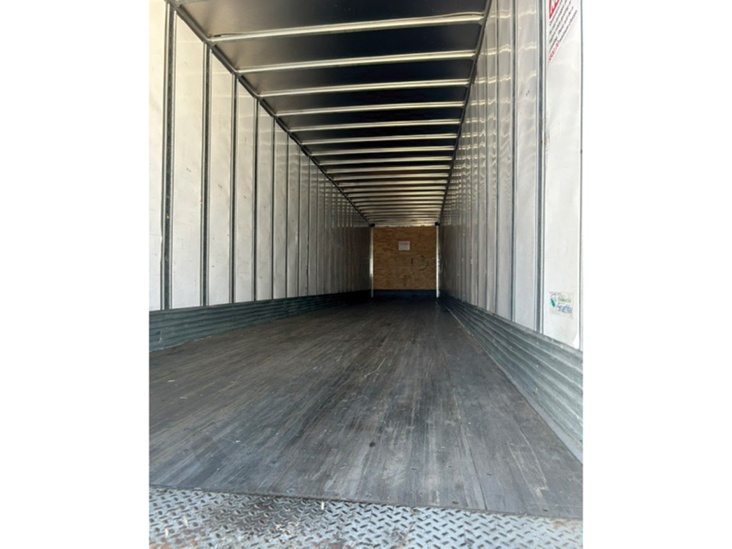 Trailer interior showing empty cargo space with metal side walls, ribbed ceiling, and wooden back wall at far end.