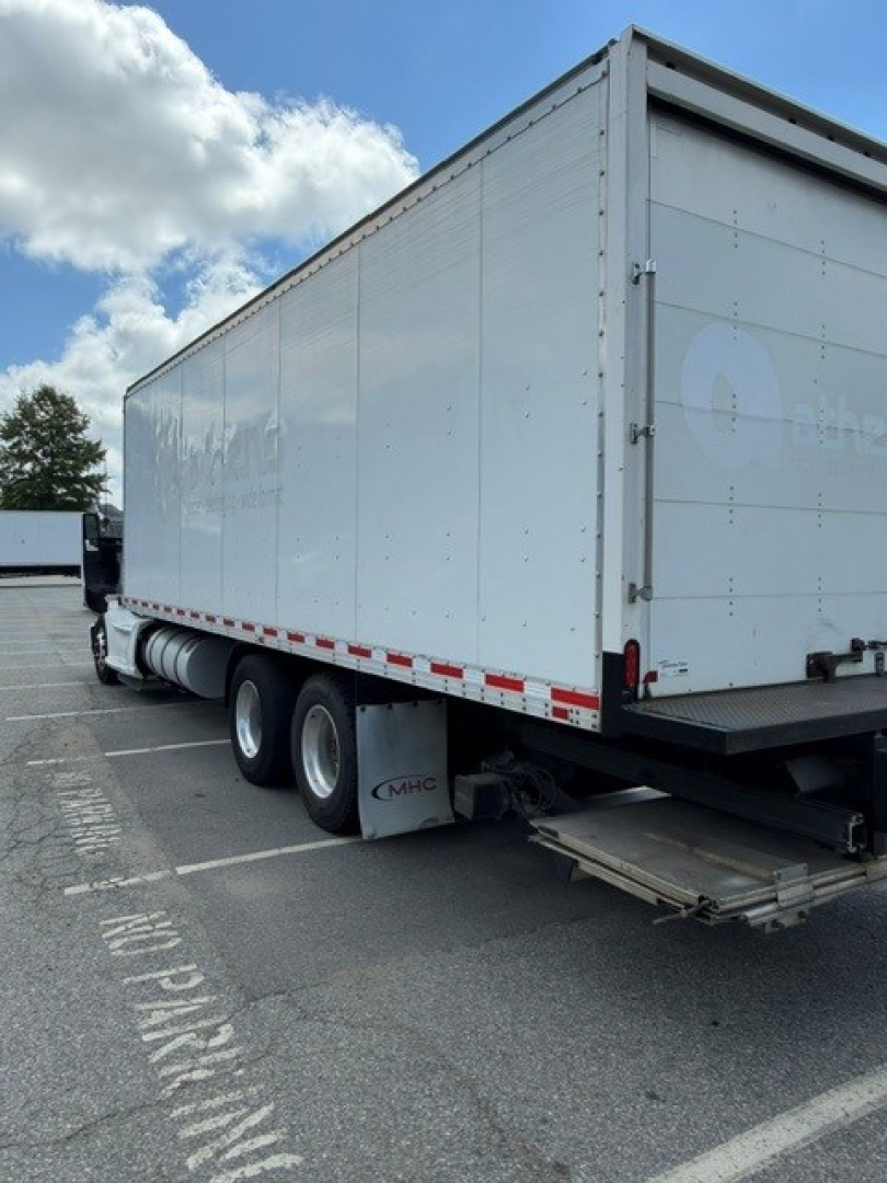 Kenworth T680 box truck trailer with raised rear, side of box shows faint logo, wheels and mudflaps visible.