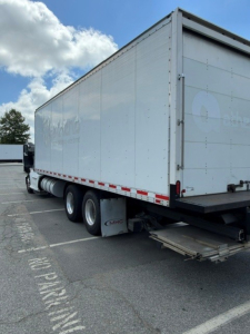 Kenworth T680 box truck trailer with raised rear, side of box shows faint logo, wheels and mudflaps visible.