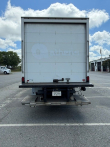 Rear view of a 2020 Kenworth T680 box truck showing back doors, taillights, and a bumper with a license plate; visible sticker and metal frame.