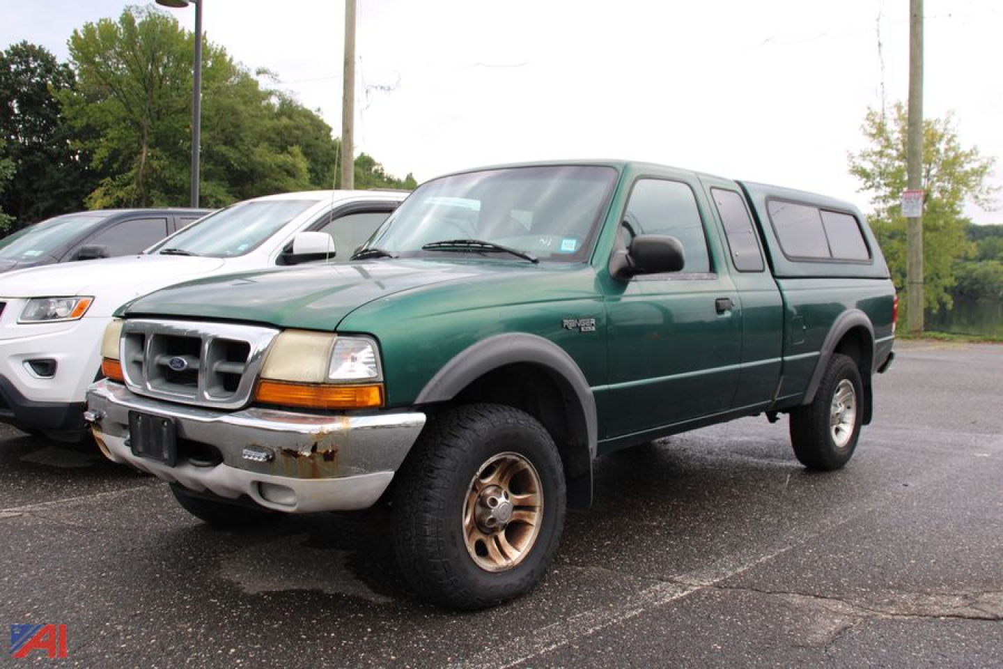 Ford Ranger pickup truck with cap, green body, gray bumper, and beige wheels in a parking lot.