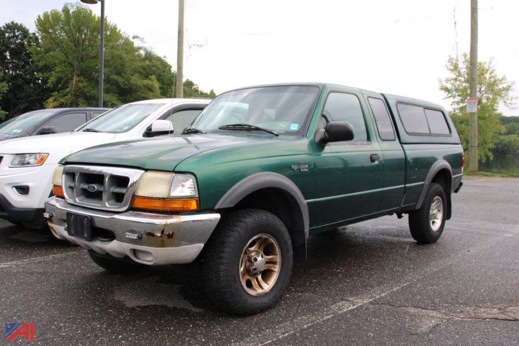 Ford Ranger pickup truck with cap, green body, gray bumper, and beige wheels in a parking lot.