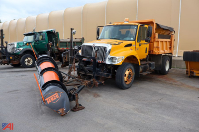 2003 International WorkStar 7300 dump truck with plow and spreader attached, yellow cab, black plow; other trucks in background.