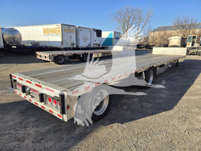 Flatbed trailer in a yard showing long deck with drop style, dual rear tandem axles, and rear lights