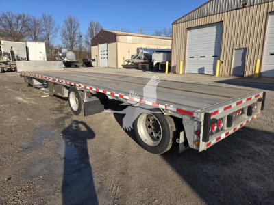Flatbed trailer in a yard showing a dropdeck platform with dual rear lights and reflective tape along edges.