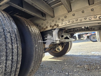 Trailer undercarriage showing suspension and frame brackets; view of dual rear wheels and underside components of a dropdeck trailer.