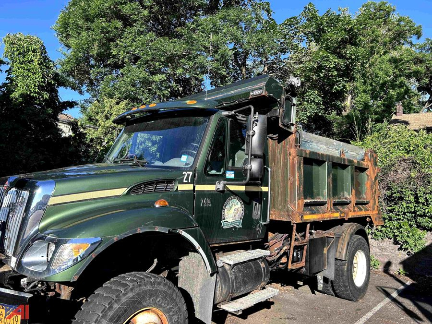 Dump truck side view showing 2004 International WorkStar 7400 with green cab and rusted dump bed, large front tire, and chrome exhaust stack.