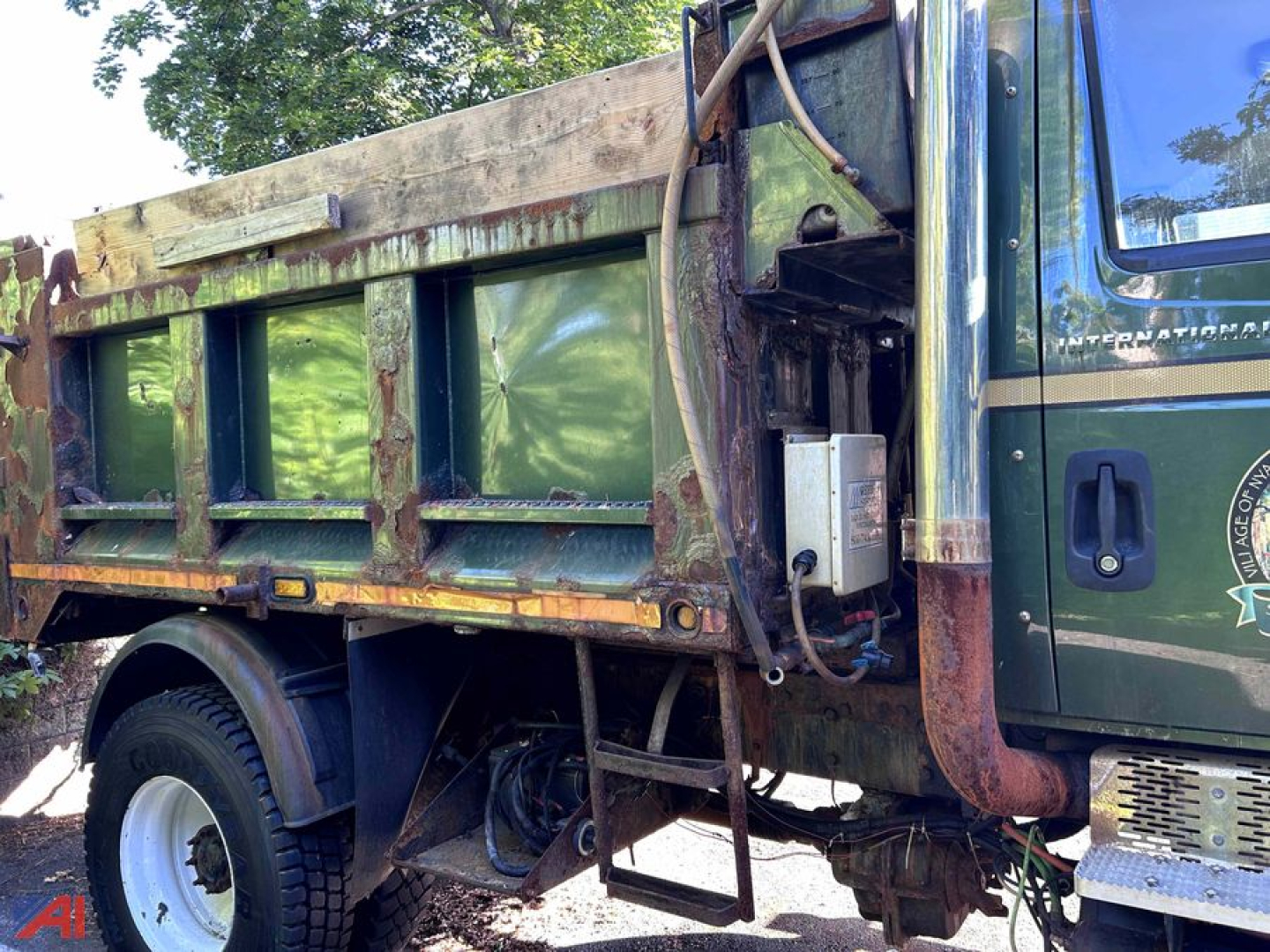 Dump truck bed and cab of a 2004 International WorkStar 7400 showing side view with green cab, rust-toned steel dump body, hydraulic components, and front wheel.