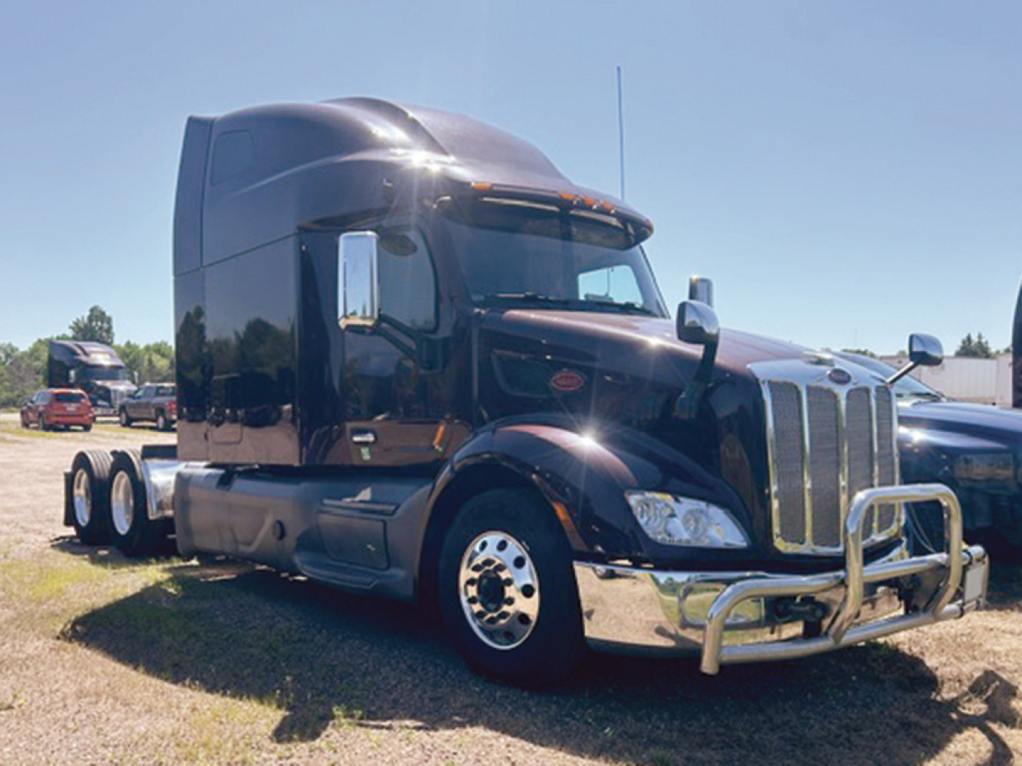 Peterbilt 579 conventional sleeper truck in dark color showing front grille, bumper guard, and side view with twin rear axles.