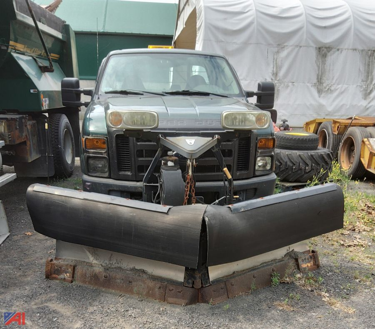 Ford F-250 Super Duty pickup with front-mounted plow, dual headlights, and heavy equipment in background.
