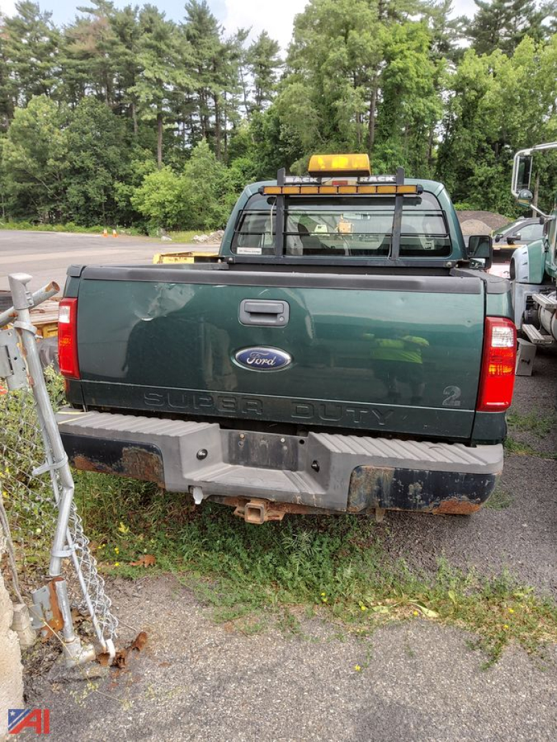 Ford F-250 Super Duty rear view with plow setup showing tailgate and bumper; green pickup with ballast weight, back windows, and Ford emblem visible.