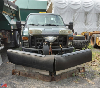 Ford F-250 Super Duty pickup with front-mounted plow, dual headlights, and heavy equipment in background.