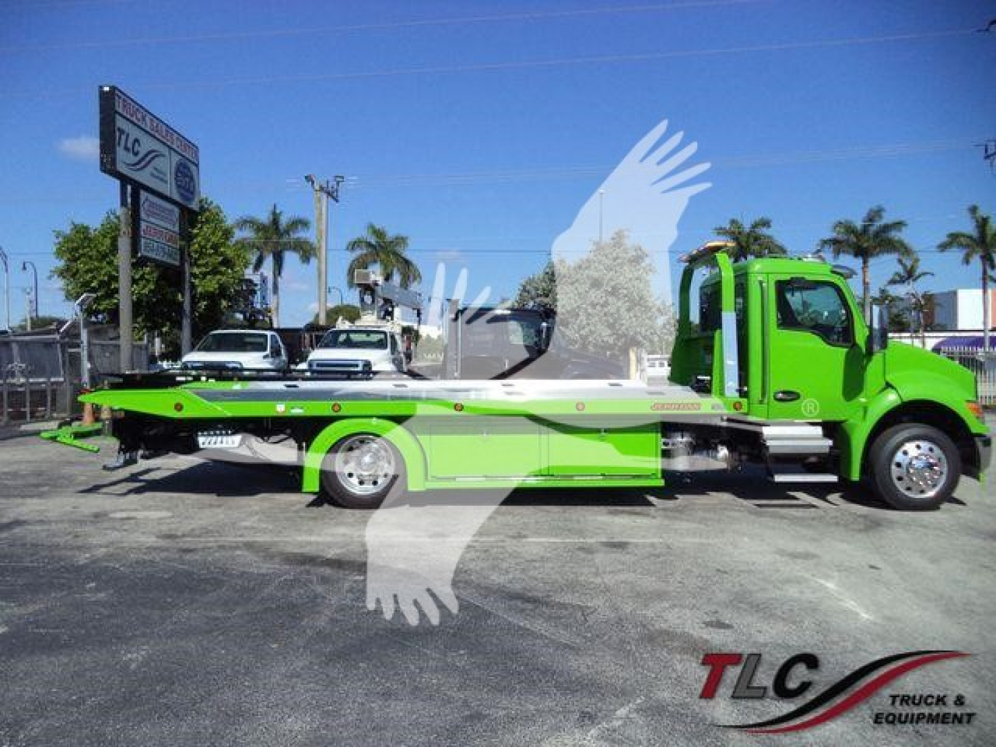 Kenworth T280 rollback tow truck in lime green and white, side view showing flatbed with hydraulic winch, branding and dealership lot in background.