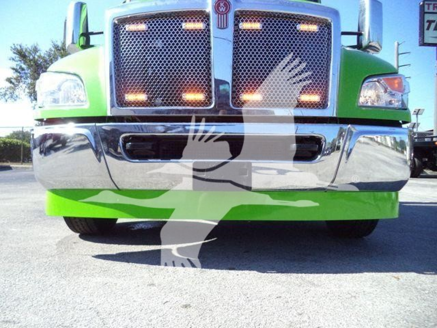 Front view of a green Kenworth T-series truck showing chrome grille and bumper; partial vehicle silhouettes overlaying the image.