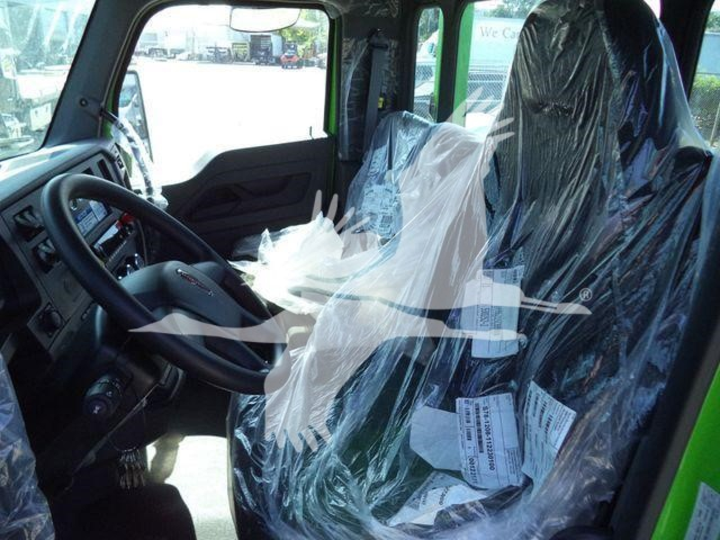 Truck cab interior of a 2025 Kenworth T280 rollback with plastic-wrapped seats and steering wheel visible.