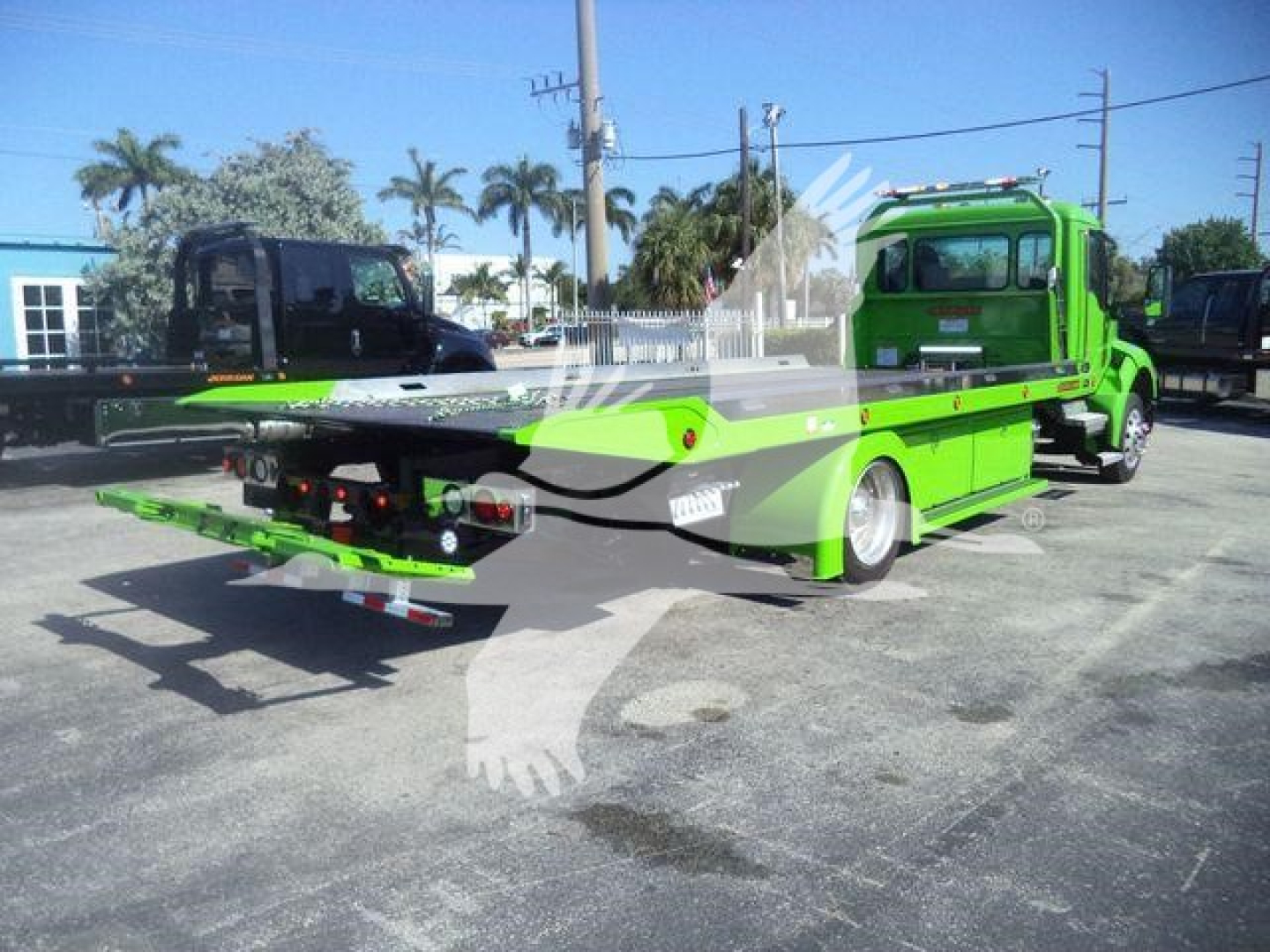 Kenworth T280 rollback truck in bright green with flatbed, rearview showing hydraulic ramps and warning labels.