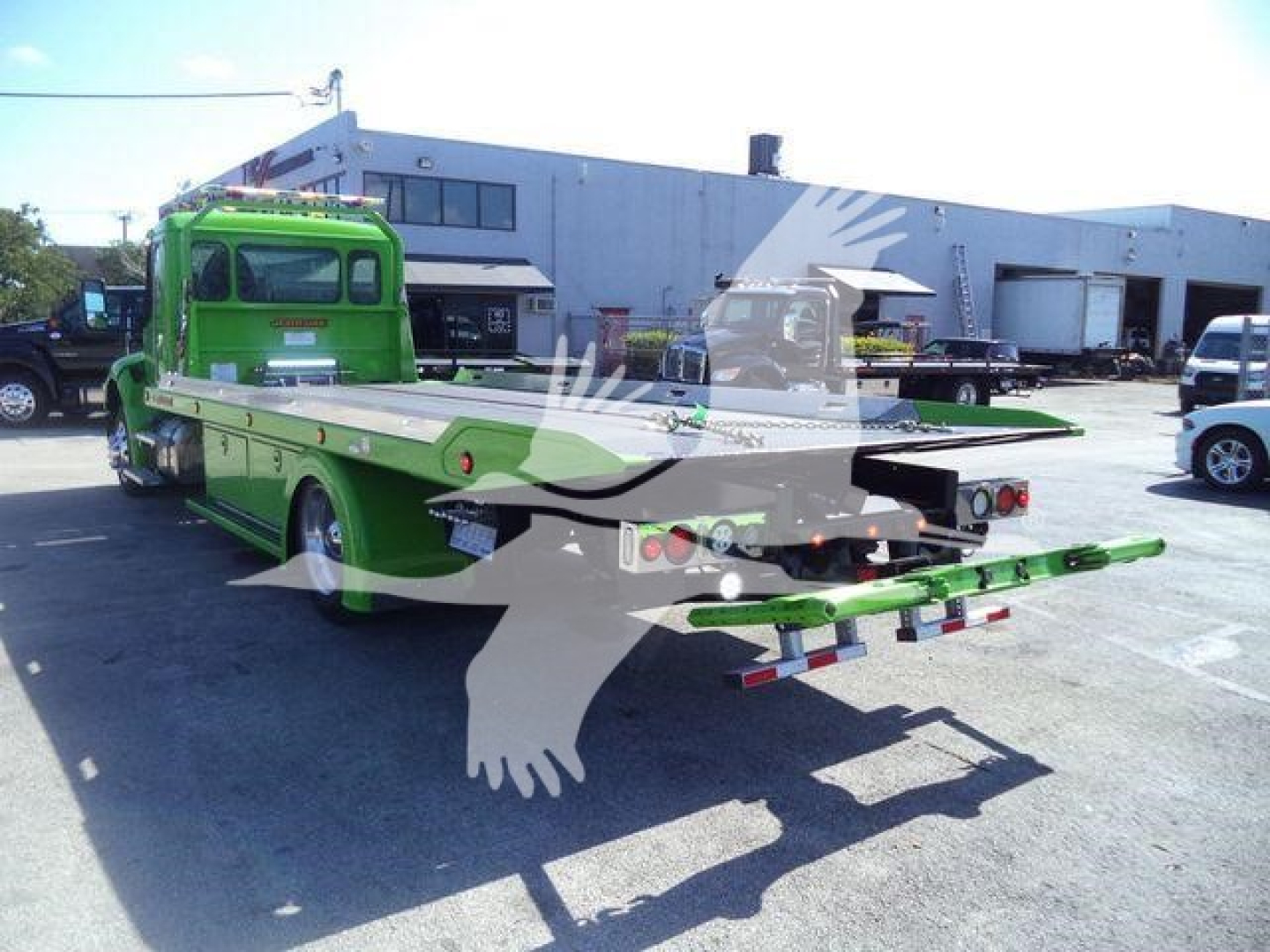 Kenworth T280 rollback truck in bright green with a flatbed and extended rear, viewed from rear-left angle in a dealership lot.