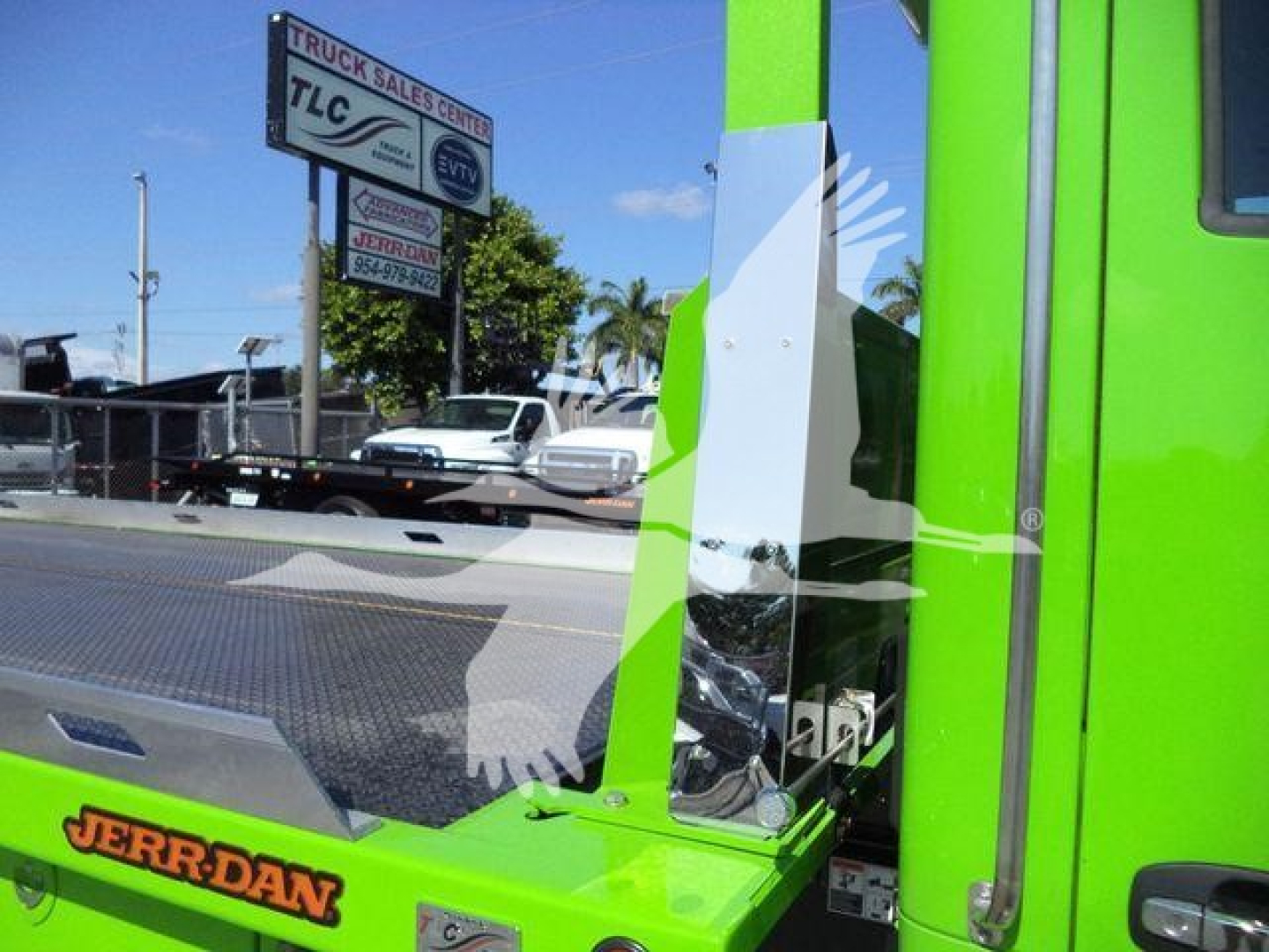 Kick panel and side view of a bright green Kenworth T280 rollback truck with metal platform and door handle, showroom lot in background.
