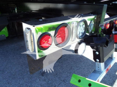 Kenworth truck rollback equipment with rear lights assembly: two red circular lights, two clear rectangular lights, and a round white light on a green reflective housing showing mounting bracket and support structure.