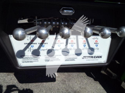Tow truck stake body tilt mechanism control panel with knobs and levers, Jerr-Dan branding visible on lower right, metallic surface with labels.