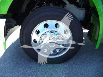 Front wheel of a green Kenworth truck showing tire and chrome hub with reflective surface.