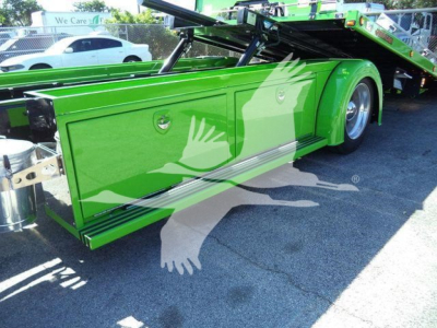 Green Kenworth T Series rollback truck side storage compartments and lower side paneling visible with glossy finish in daytime.